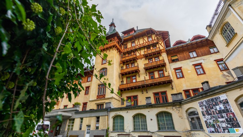 Südbahnhotel Semmering, © Wiener Alpen - Kremsl Historisches Gebäude des Südbahnhotels Semmering mit Holzverzierungen und Balkonen, umgeben von grünen Pflanzen.