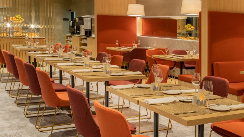 Restaurant, © Hilton Garden Inn Wiener Neustadt Innenansicht eines modernen Restaurants mit gedeckten Tischen und roten Stühlen.