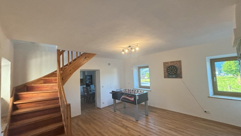 Gemeinschaftsraum mit Wuzzler und Dartscheibe, © Wiener Alpen Ein Gemeinschaftsraum mit Tischfußballtisch, Dartscheibe an der Wand, Holztreppe und zwei Fenstern.