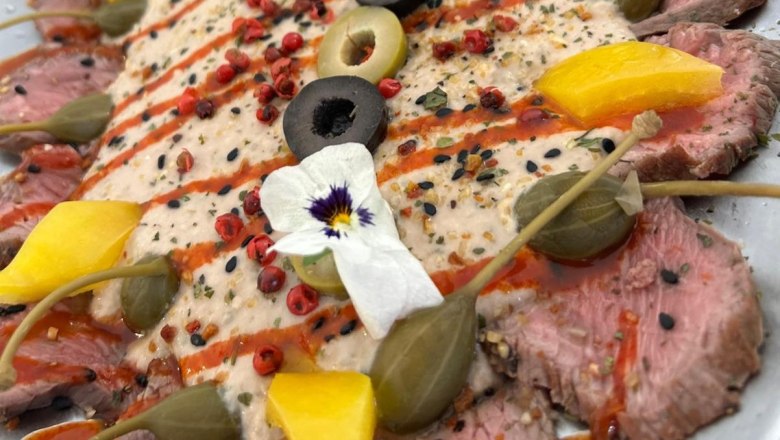 Fine meat at the Freiherr, © Markus Jokesz Close-up of a decorative plate of pink, finely chopped meat with capers, olives and edible flowers.