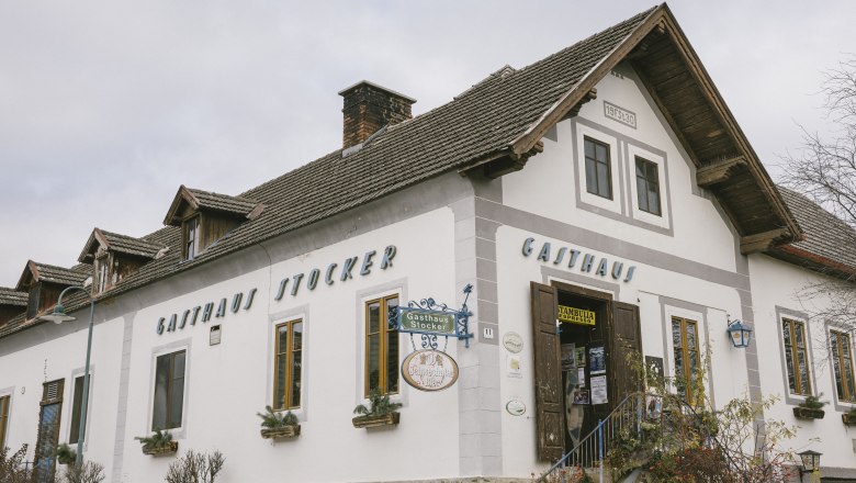 Kräuterwirtin Gerda Stocker Landgasthof mit Gastgarten, © Wiener Alpen/Sophie Menegaldo Außenansicht des Gasthauses Stocker mit Eingangstreppe und Werbeschildern.