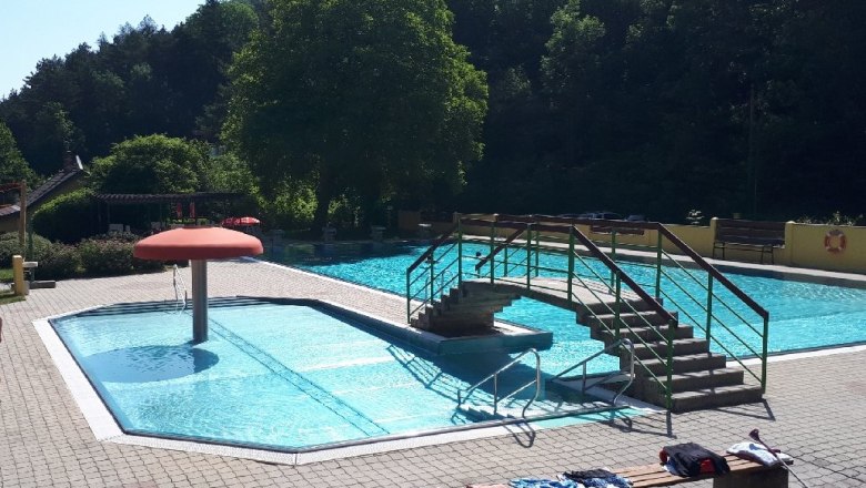 Solarfreibad Waldegg,, © (c) Gemeinde Waldegg Ein Freibad mit einem kleinen Pool, einer Brücke und einem Pilz-Wasserspiel. Umgeben von Bäumen und einem sonnigen Himmel.