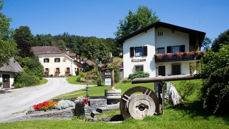 Gästehaus, © Gästehaus Buchegger, Foto Buchegger Ein ländliches Gästehaus mit Blumen und einem alten Mühlstein im Vordergrund.