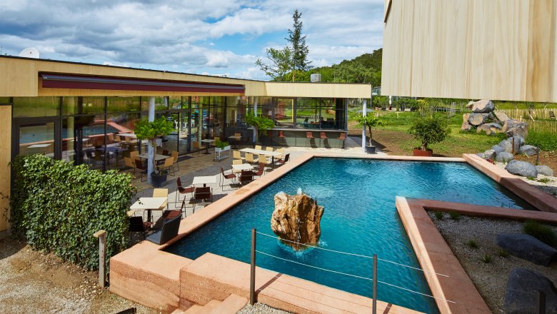 Veranda: Breakfast and snack by a water lily pond, © Gut Guntrams- Picasa Modern terrace with tables and chairs next to a rectangular pond with rocks in the middle.