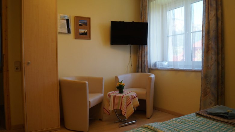 Sitzgruppe im Ahornzimmer, © Reep Gemütliche Sitzecke mit zwei Sesseln, kleinem Tisch und Fernseher in einem hellen Raum mit Fenster.