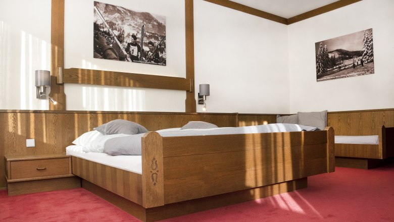 Double bed, © Doris Seebacher A bedroom with a wooden double bed, red carpeting and two black and white pictures on the wall.