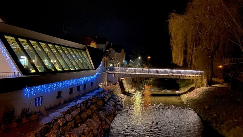 Höfler by the river at night, © Wiener Alpen Night scene with illuminated modern building and river.