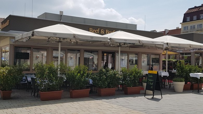 Reef & Beef Schanigarten, © Piroska Weiss Außenansicht eines Restaurants mit Schanigarten und Sonnenschirmen.