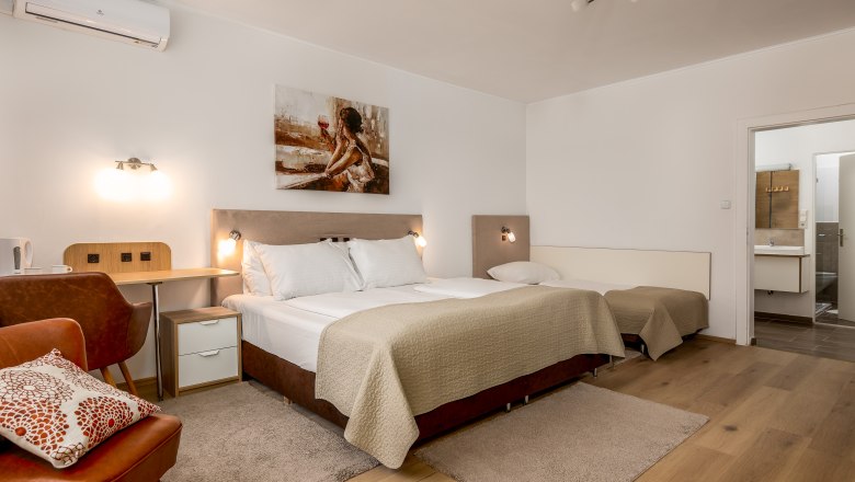 Hotel Zentral Dreibettzimmer, © MartinHaider Fotografie/Hotel Zentral Schwartz GmbH Dreibettzimmer in einem Hotel mit Doppelbett, Einzelbett, Schreibtisch und Badezimmer.