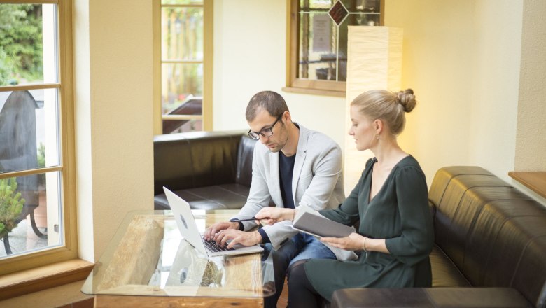 Alpen-Aktiv-Landgasthof zur Schubertlinde, © Patrick Haberler Zwei Personen arbeiten an einem Laptop in einem gemütlichen Raum mit großen Fenstern.