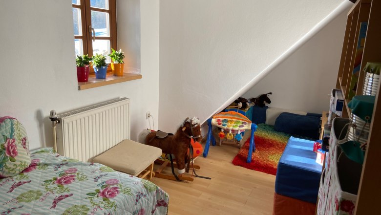 Kinderzimmer mit Spieleecke, © Wiener Alpen Kinderzimmer mit Bett, Spielzeug und buntem Teppich.