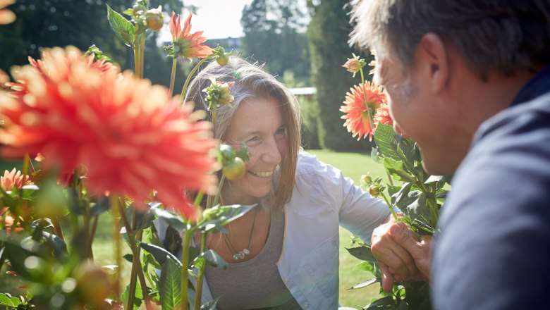 Kurpark Bad Schönau, © Wiener Alpen, Florian Lierzer Zwei Personen lächeln sich zwischen blühenden Dahlien im Freien an.