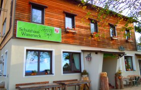 Eingang zum Schutzhaus Waxeneck, © Waxeneckhaus Eingang zum Schutzhaus Waxeneck mit Holztischen und Blumenkästen.