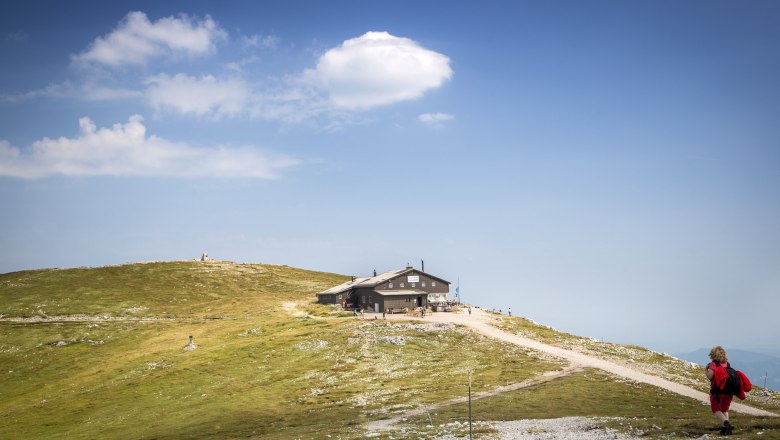 Blickplatz Fischerhütte Schneeberg, © Wiener Alpen, Foto: Franz Zwickl Eine Berghütte auf einem Hügel mit blauem Himmel und Wolken im Hintergrund.