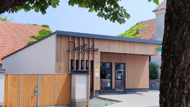 Dorfladen Lichtenegg, © Wiener Alpen Ein moderner Dorfladen mit Holzfassade und Schildern, umgeben von Bäumen.