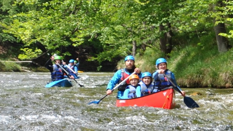 Kanu Kayak Wildnis Zentrum Nasswald, © Georg Bergthaler Menschen in Kanus paddeln auf einem Fluss in einer grünen Waldlandschaft.