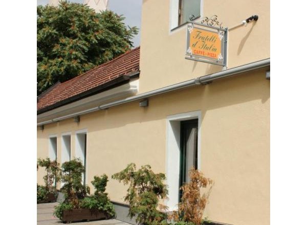 mit Schanigarten, © Herold Außenansicht eines gelben Gebäudes mit einem Schild "Fratelli d'Italia Caffè-Pizza" und Pflanzen vor der Fassade.