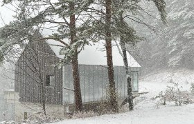 Caspar´s Home im Winter, © Meinrad Hofer Ein modernes Haus im Wald, umgeben von Schnee und Bäumen, während es stark schneit.