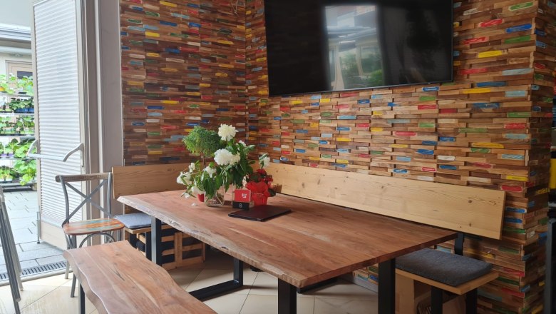 Siegl's Pub, © Siegl's Pub Innenansicht eines Pubs mit Holztisch, Bank und bunter Holzverkleidung an der Wand.