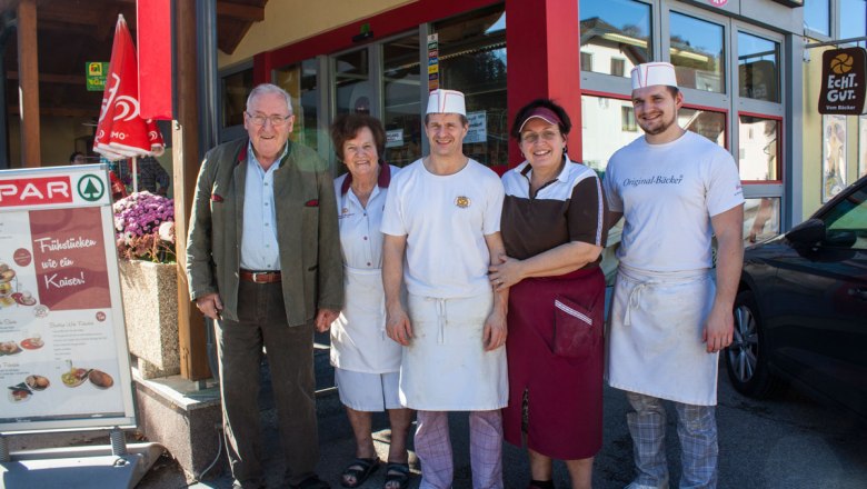 Family Bernhard & Birnbauer, © Clemens Trenker, BA Five people stand smiling in front of a store entrance.