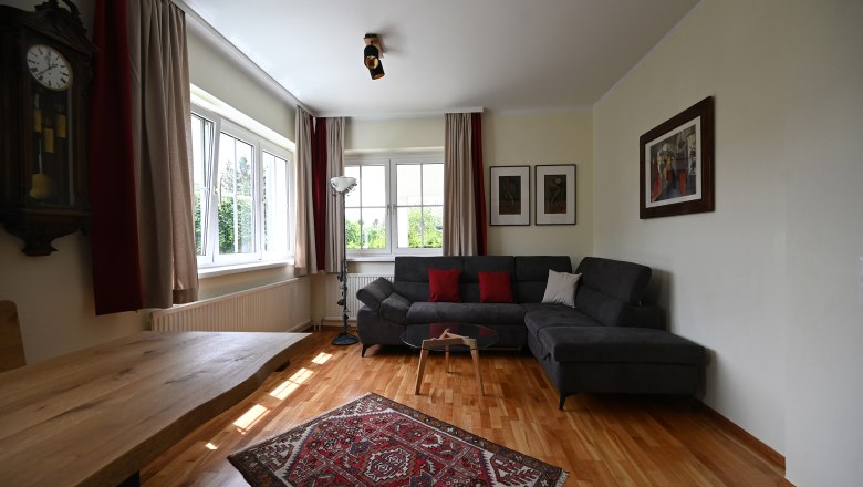 Wohnzimmer, © Christine Kuppelwieser Modernes Wohnzimmer mit grauem Sofa, Holztisch, Teppich und Wanduhren.