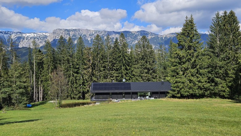 Walddenke, Hausansicht, © Mag. Plötzeneder Modernes Haus mit Solarpanelen vor einem Wald und Bergen im Hintergrund.