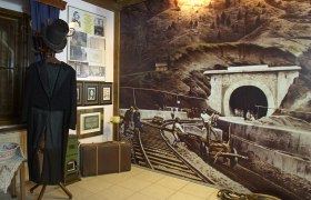 Ausstellungsräume Ghega Museum, © Wiener Alpen, Foto: Bene Croy Innenansicht des Ghega Museums mit historischem Anzug, Bildern und einer großen Wandmalerei eines Eisenbahntunnels.