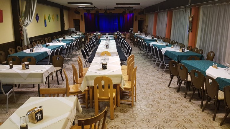 Veranstaltungssaal Wirtshausbühne Bernhart, © Wirtshausbühne Bernhart Ein leerer Veranstaltungssaal mit gedeckten Tischen und einer Bühne im Hintergrund.