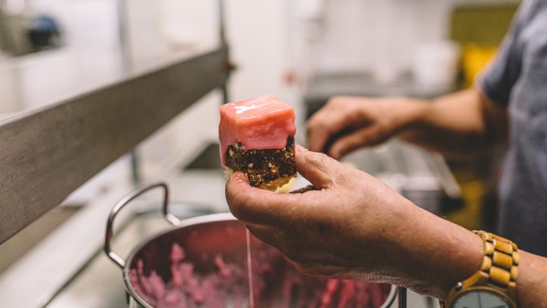 Baking and cooking courses are offered, © Niederösterreich Werbung/Mara Hohla Person holding a piece of pastry with pink icing over a pot.