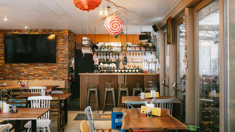 Siegl's am Markt, © Wiener Alpen/Sophie Menegaldo Innenansicht eines gemütlichen Cafés mit Holztischen, Barhockern und einer dekorativen Bar.