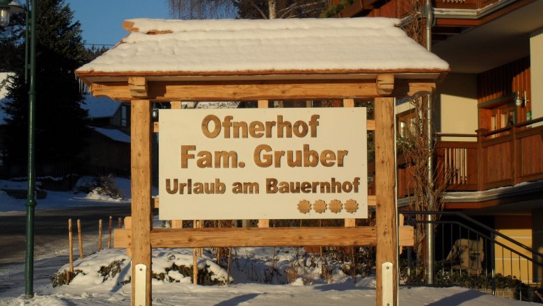 Willkommen, © ©Ofnerhof Holzschild mit der Aufschrift 'Ofnerhof Fam. Gruber Urlaub am Bauernhof' im Schnee.