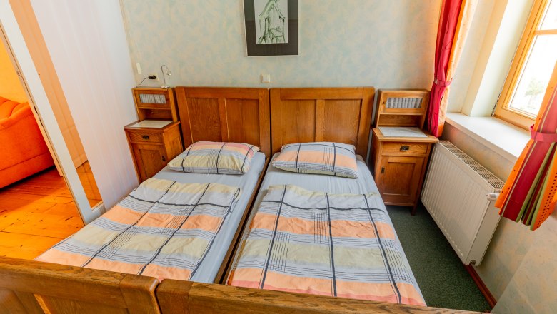 Bedroom, © Wiener Alpen / Christian Kremsl A bedroom with two single beds, wooden furniture and a window with red curtains.