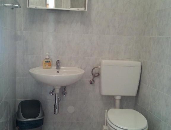 Badezimmer, © Haus Nova Kleines Badezimmer mit Waschbecken, Spiegel, Toilette und Mülleimer.