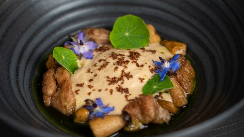 Enjoyment is not neglected, © Sporthotel Semmering An elegant dish in a black bowl, decorated with edible flowers and green leaves.