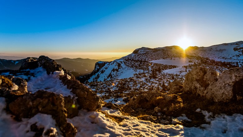Stille Winkel am Rax-Plateau, © Wiener Alpen/Kremsl Sonnenuntergang über schneebedecktem Rax-Plateau mit Felsen im Vordergrund.