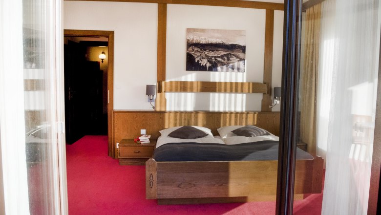 Room, © Doris Seebacher A cozy bedroom with a double bed, wooden furniture and a picture on the wall. The floor is covered with a red carpet.