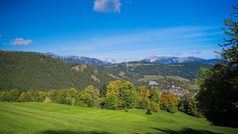 Schneebergblick Golfplatz Semmering, © Alexander Kramel Blick auf eine grüne Landschaft mit Hügeln und Bergen im Hintergrund, unter einem klaren blauen Himmel.