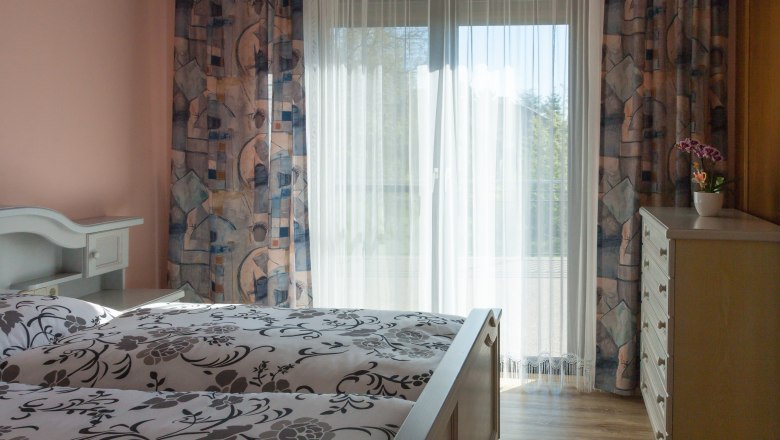 Schlafzimmer, © Fam. Sulzbacher Helles Schlafzimmer mit Bett, Vorhängen und Kommode.
