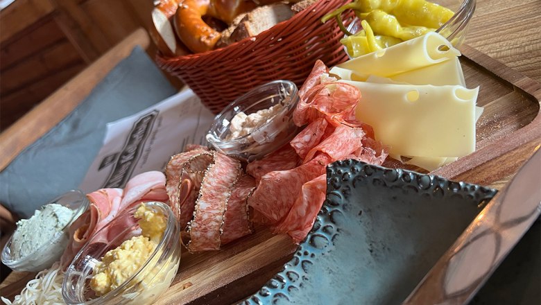 old-cellar-house-katzelsdorf, © altes-kellerhaus.at A rustic snack with sausage, cheese, bread and spreads on a wooden plate.