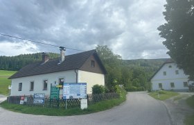Ferienhaus Hofer, © Michael Hofer Ländliche Straße mit zwei Häusern und Wegweisern, umgeben von Wäldern und Wiesen.