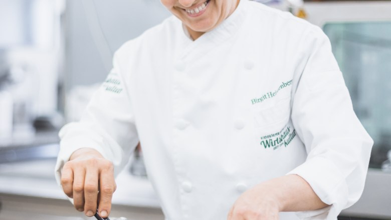 Birgit Heissenberger, © Niederösterreich Werbung/David Schreiber Egy fehér egyenruhás szakács egy profi konyhában serpenyőben sült ételt süt.