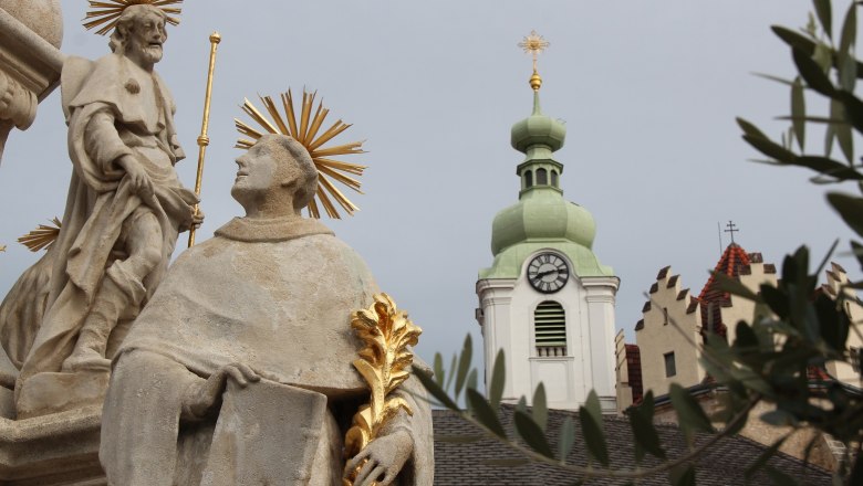 Kirche, Dreifaltigkeit, © Stadtgemeinde Neunkirchen Statue mit Heiligenschein vor Kirchturm mit Uhr und grünem Dach.