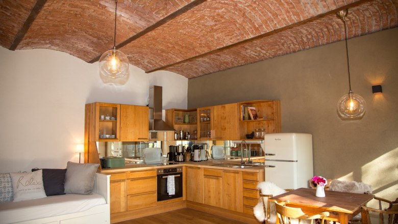 Wohnküche Ferienwohnung Lindner, © Magdalena Hirsch Gemütliche Küche mit Holzmöbeln, Ziegeldecke und Esstisch.