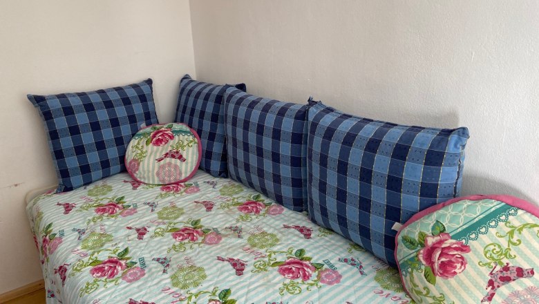 Kinderzimmer mit Ausziehbett, © Wiener Alpen Ein Kinderzimmer mit einem Ausziehbett, das mit einer geblümten Decke und blauen Kissen dekoriert ist.