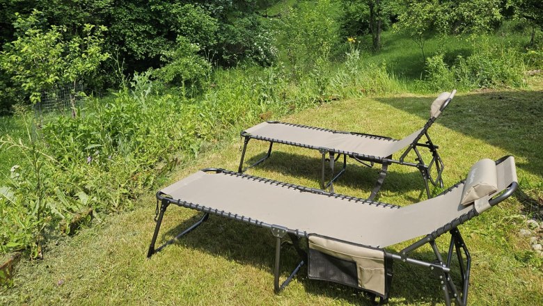 Orlet an der Rax, © Sofia Orlet Zwei Liegestühle auf einer Wiese mit Blick auf bewaldete Berge unter blauem Himmel.