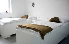 Arbeiterquartier UHL, © Arbeiterquartier UHL Zwei weiße Betten in einem hellen Raum mit braunen Decken und Kissen.