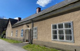 Ferienwohnung Pleesz, © Wiener Alpen Langes, einstöckiges Gebäude mit mehreren Fenstern und einem Schrägdach unter blauem Himmel.