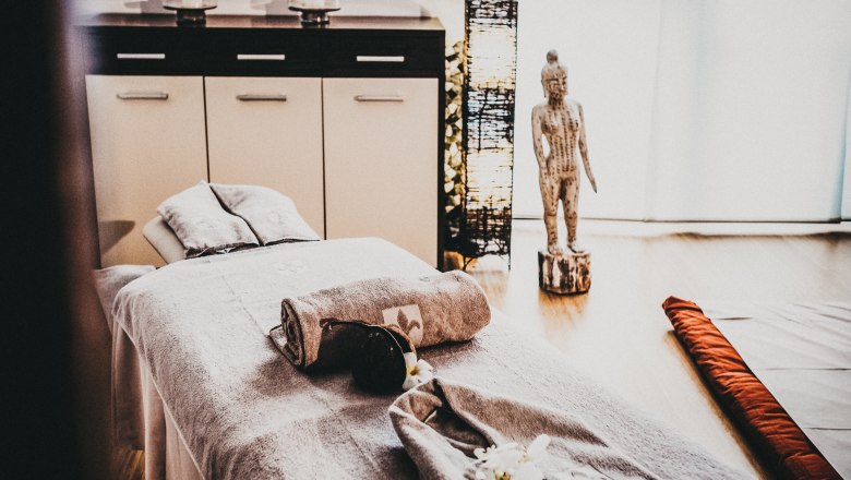 Spa Bereich Linsberg Asia, © Linsberg Asia Ein Spa-Raum mit Massageliege, Handtüchern, Buddha-Statue und Kerzen.