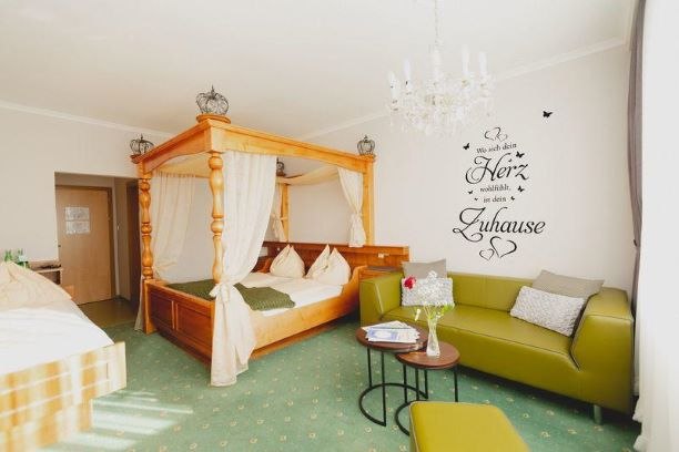 Four-poster room, © Gasthof Berghof A cozy room with a four-poster bed, green couch and wall tattoo.