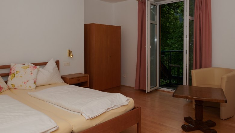 Schlafzimmer, © Landhaus Puchbergerhof by smc Schlafzimmer mit Doppelbett, Schrank, Tisch und Stuhl, Fenster mit Vorhängen.